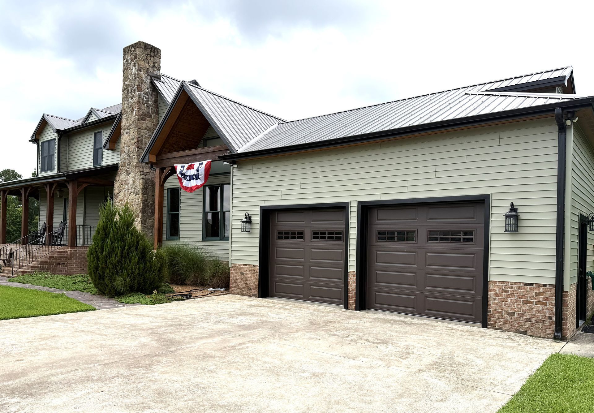 Suburban house exterior with stone chimney, double garage, and an American flag by the front door Suburban house exterior with stone chimney, double garage, and an American flag by the front door