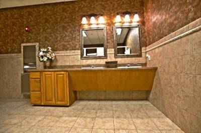 Public restroom sink area with two mirrors, wood cabinets, beige tile floor, and floral wall decor