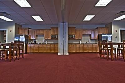 Empty cafeteria with red carpet, wooden counters, and tables under fluorescent lights