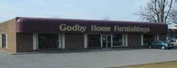 Godby Home Furnishings storefront in a strip mall parking lot, with a purple facade and large sign.