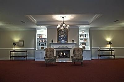 Formal living room with fireplace, two armchairs, side tables, wall sconces, and burgundy carpet.
