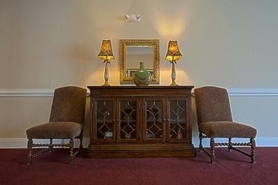Two brown chairs flank a wooden cabinet with lamps and a mirror against a beige wall.
