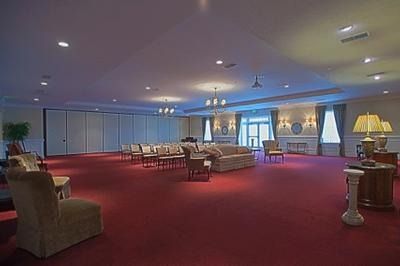 Large lounge with red carpet, sofas, armchairs, and lamps under a blue ceiling with windows at the back