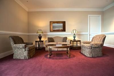 Living room with burgundy carpet, beige sofa and armchairs, coffee table, and two side tables with lamps