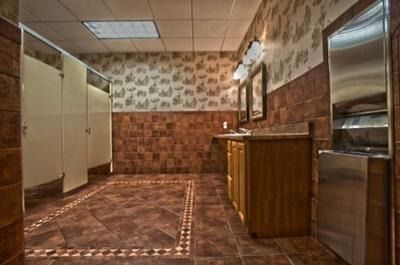 Empty public restroom with beige stalls, tiled walls and floor, and a stainless-steel hand dryer.