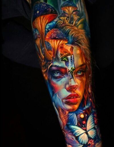 A vibrant, surreal tattoo featuring a face merged with glowing mushrooms, a small waterfall, and a butterfly in blue tones.