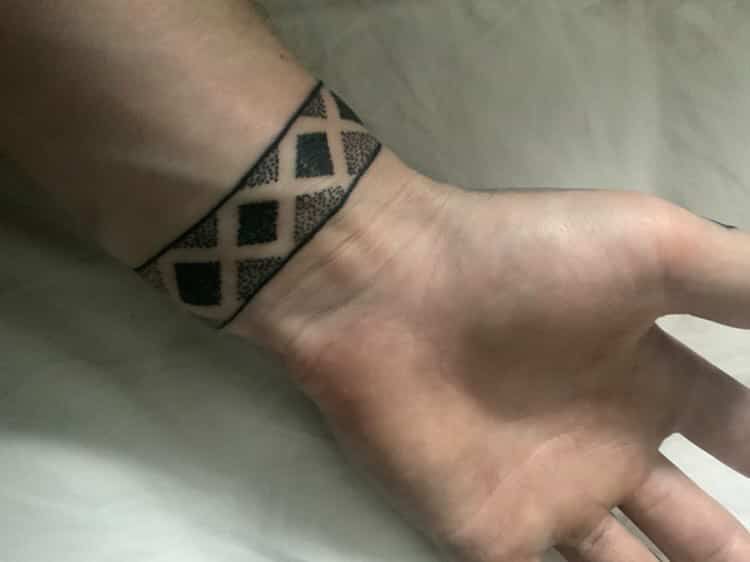 A black ink tattoo around a wrist featuring a repeating geometric diamond pattern with solid and stippled shading.