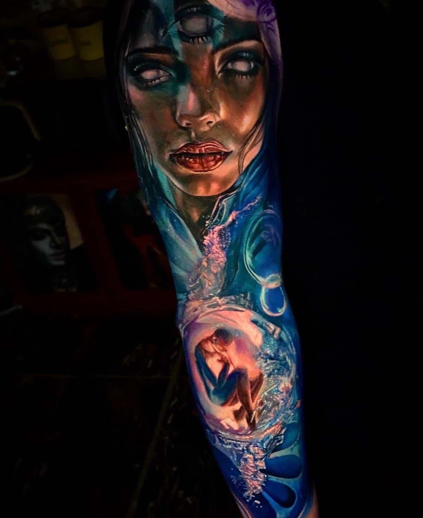 A colorful, surreal tattoo on an arm featuring a person’s face with a third eye and a small figure floating in water below.