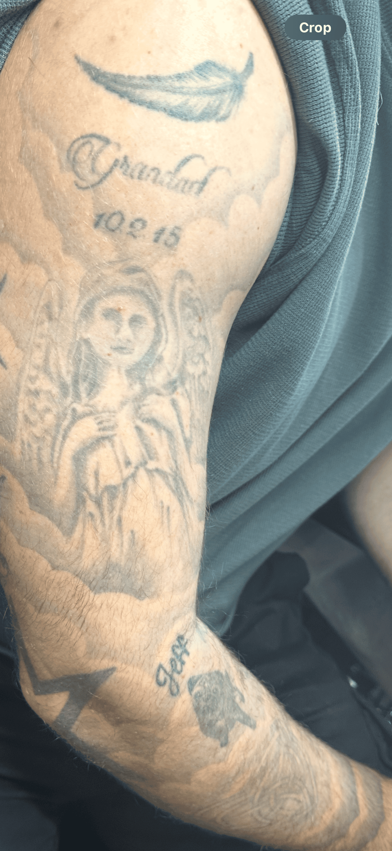 A close-up view of an arm covered in multiple tattoos, including an angel, a feather, and names with dates.