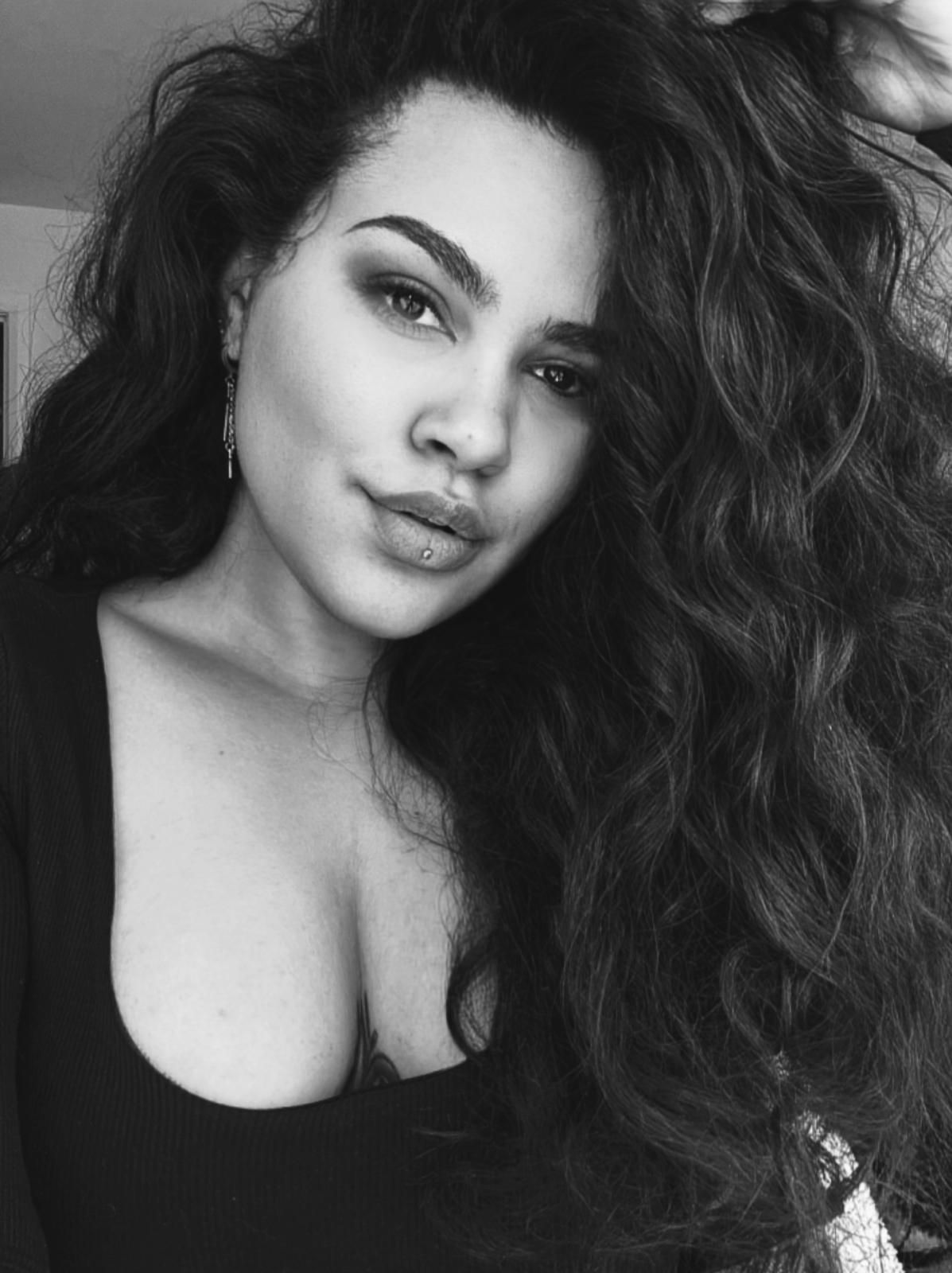 A black and white portrait of a person with long, voluminous wavy hair looking at the camera with a neutral expression.
