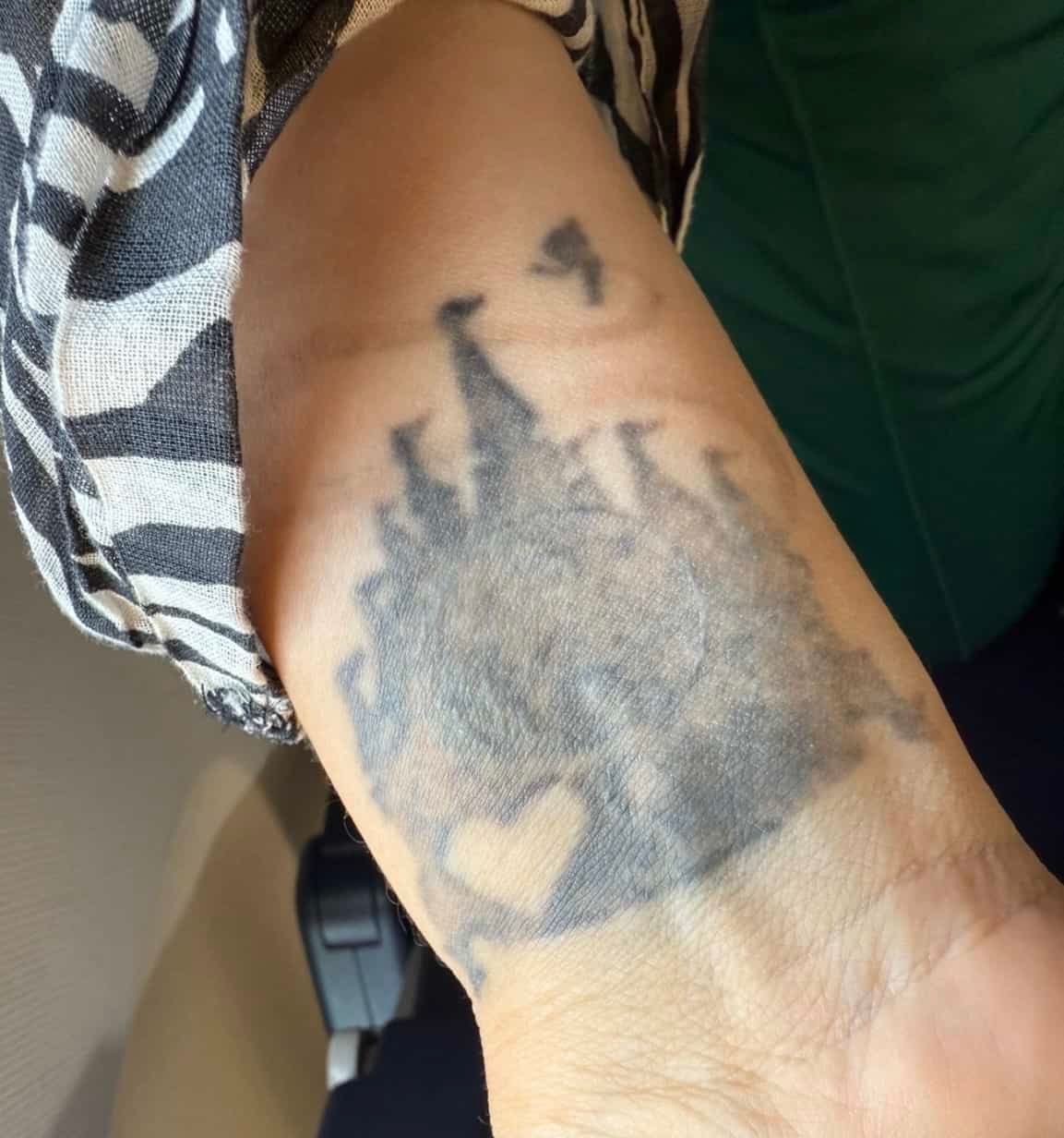 A black ink tattoo on a person's wrist featuring the silhouette of a fairy tale castle with a small heart shape at the base.