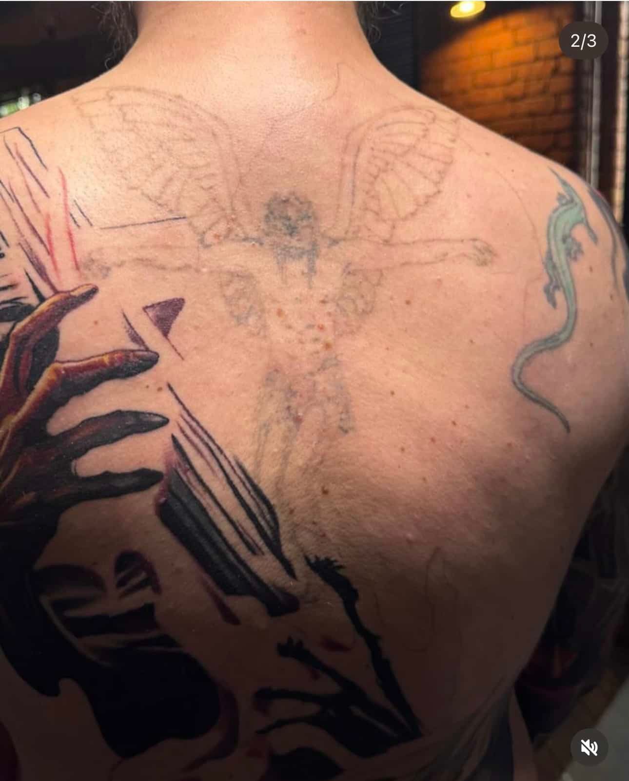 A back with a large dark abstract tattoo on the left, a faded angel outline in the center, and a small blue lizard tattoo.