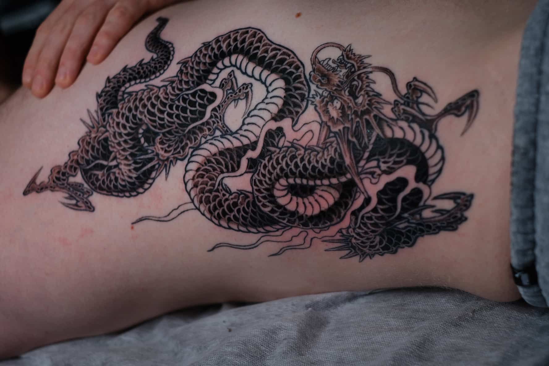 Intricate black-ink dragon tattoo wrapping across the side of a person’s torso.