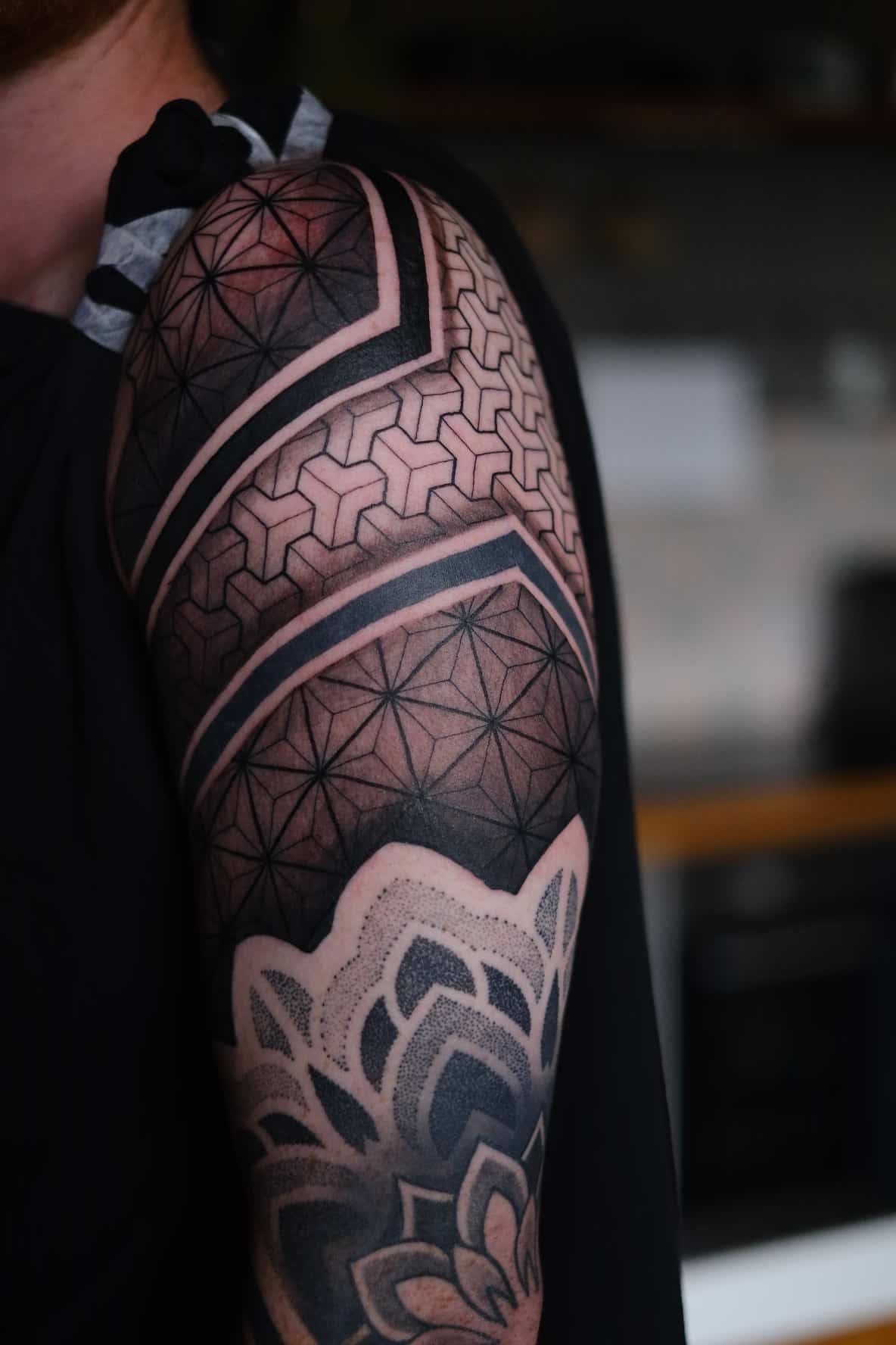 Geometric blackwork tattoo covering an upper arm, featuring intricate patterns, bold lines, and dotwork shading.