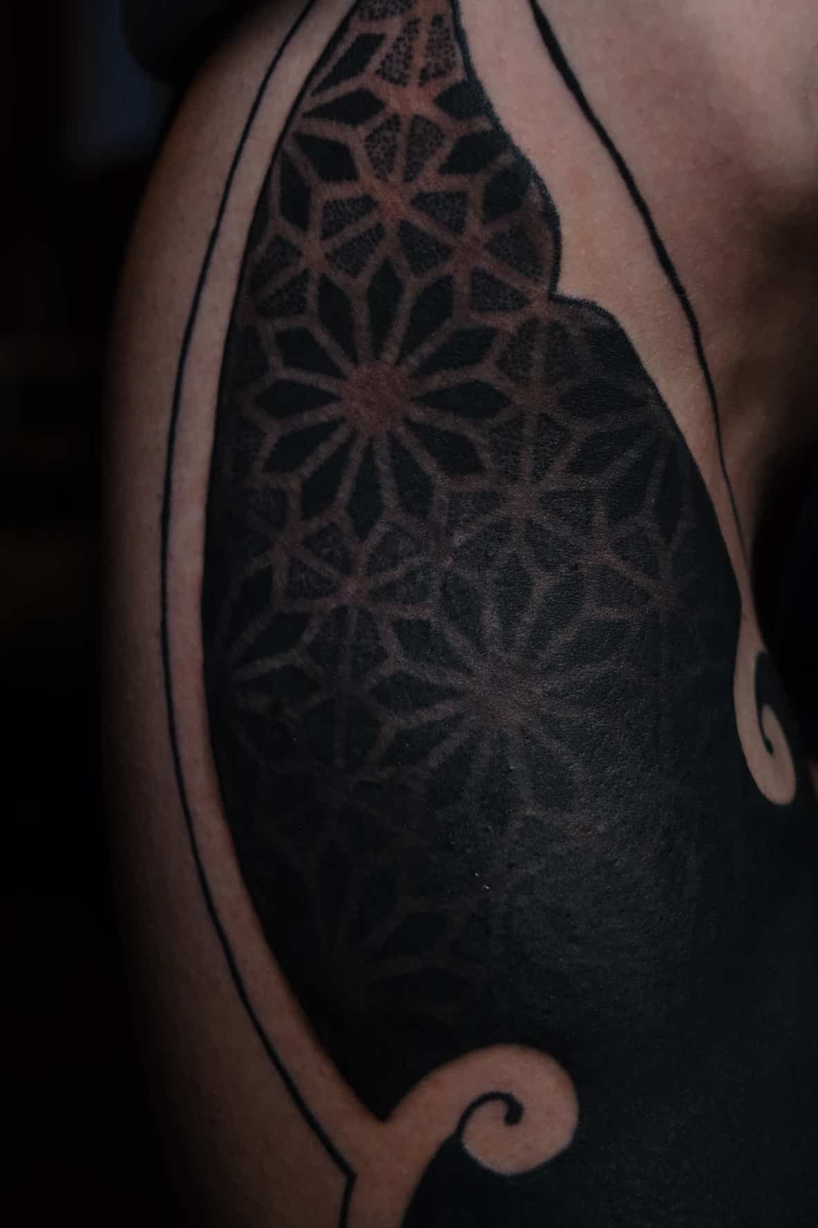A close-up of a blackwork tattoo featuring intricate, repeating geometric star patterns contrasted against solid black ink.