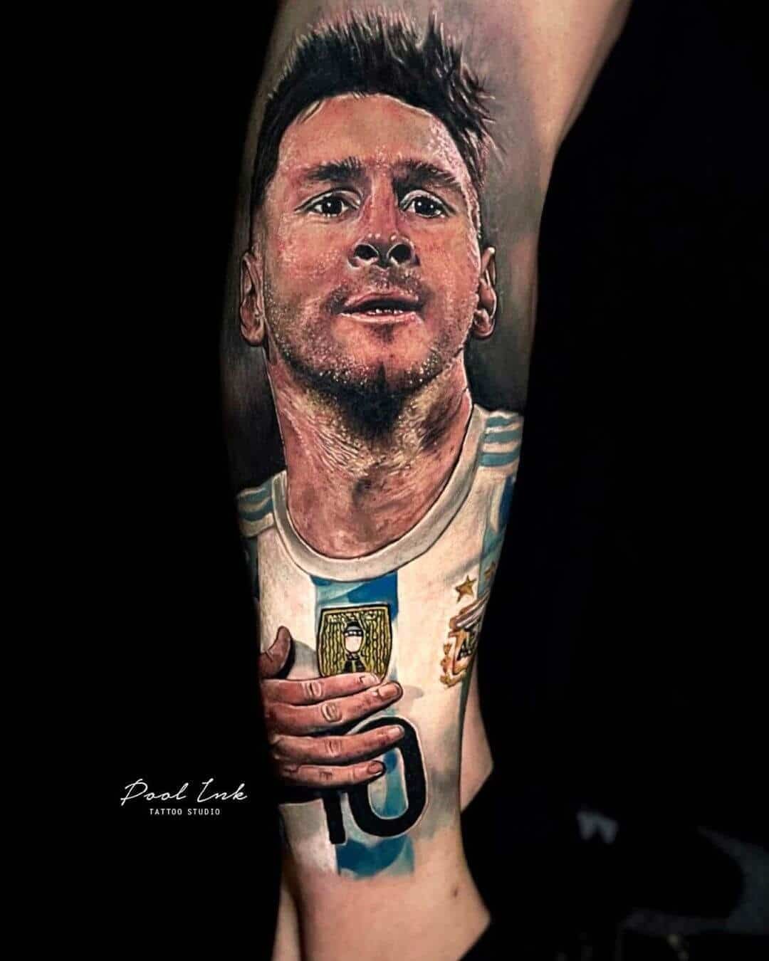 A realistic tattoo of Lionel Messi in his Argentina kit, shown from the chest up, with his hand resting on his jersey.