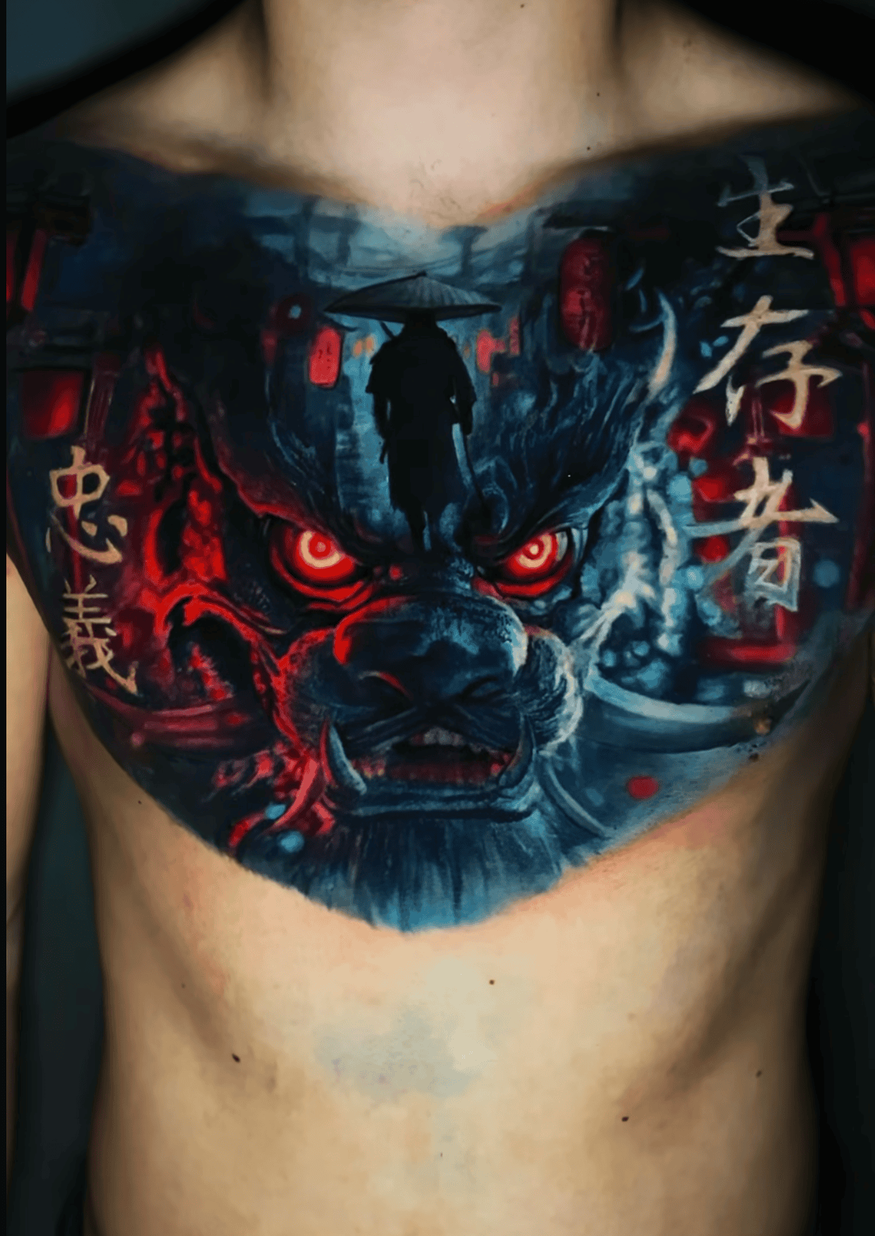 A chest tattoo featuring a fierce creature with glowing red eyes, a silhouetted figure in a hat, and stylized Kanji text.