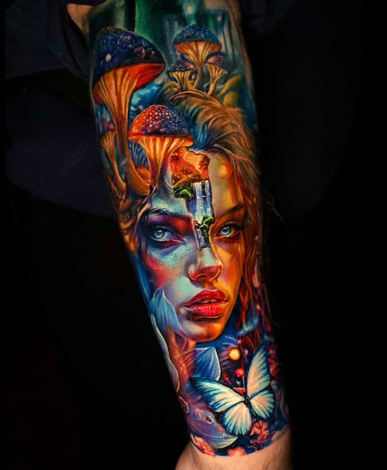 Vibrant color tattoo of a face merging with mushrooms, a small waterfall, and a glowing butterfly on a forearm.