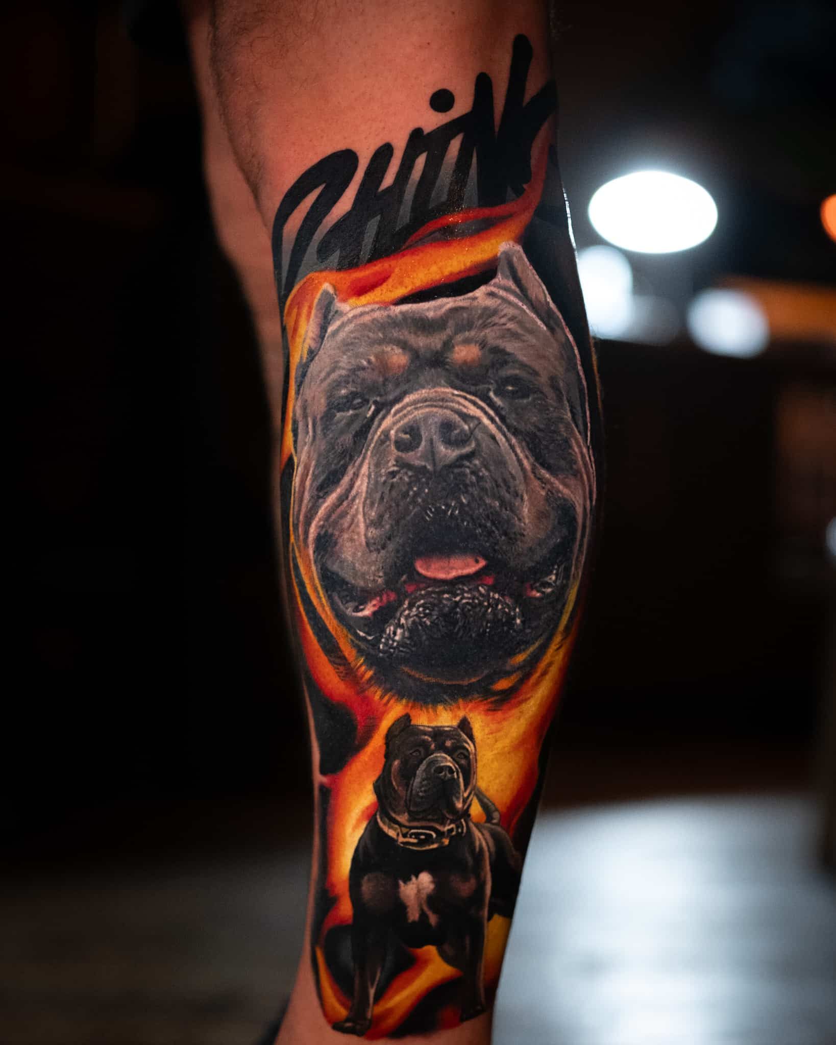 A tattoo on a leg featuring a close-up dog portrait above a full-body dog, both surrounded by orange and yellow flames.