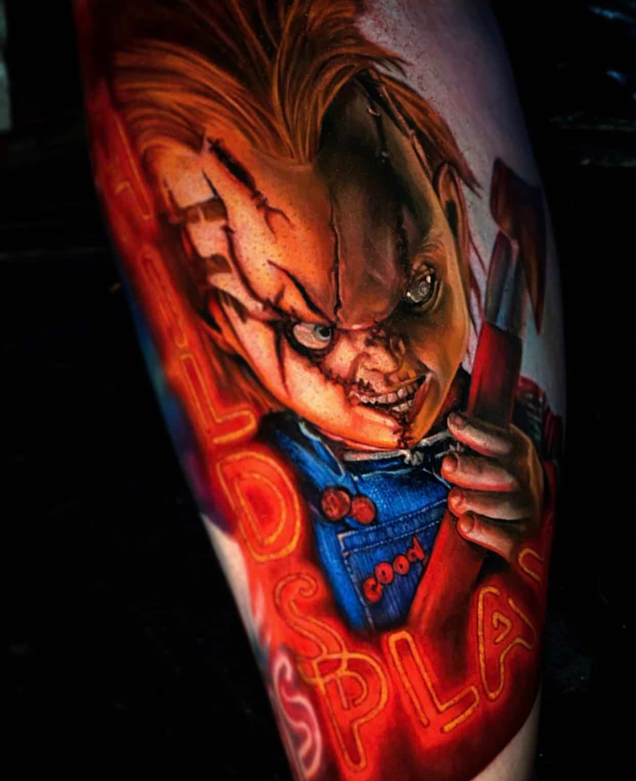 A colorful tattoo of the horror character Chucky with a menacing grin, holding a tool, framed by glowing red neon text.