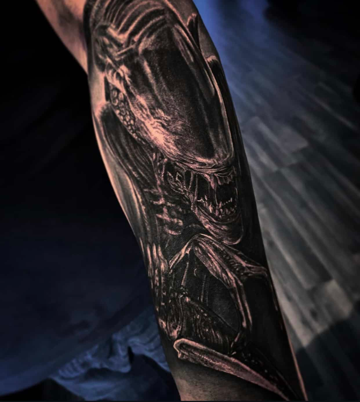 Black and gray forearm tattoo of the Xenomorph from the Alien franchise, featuring its iconic head and bared teeth.