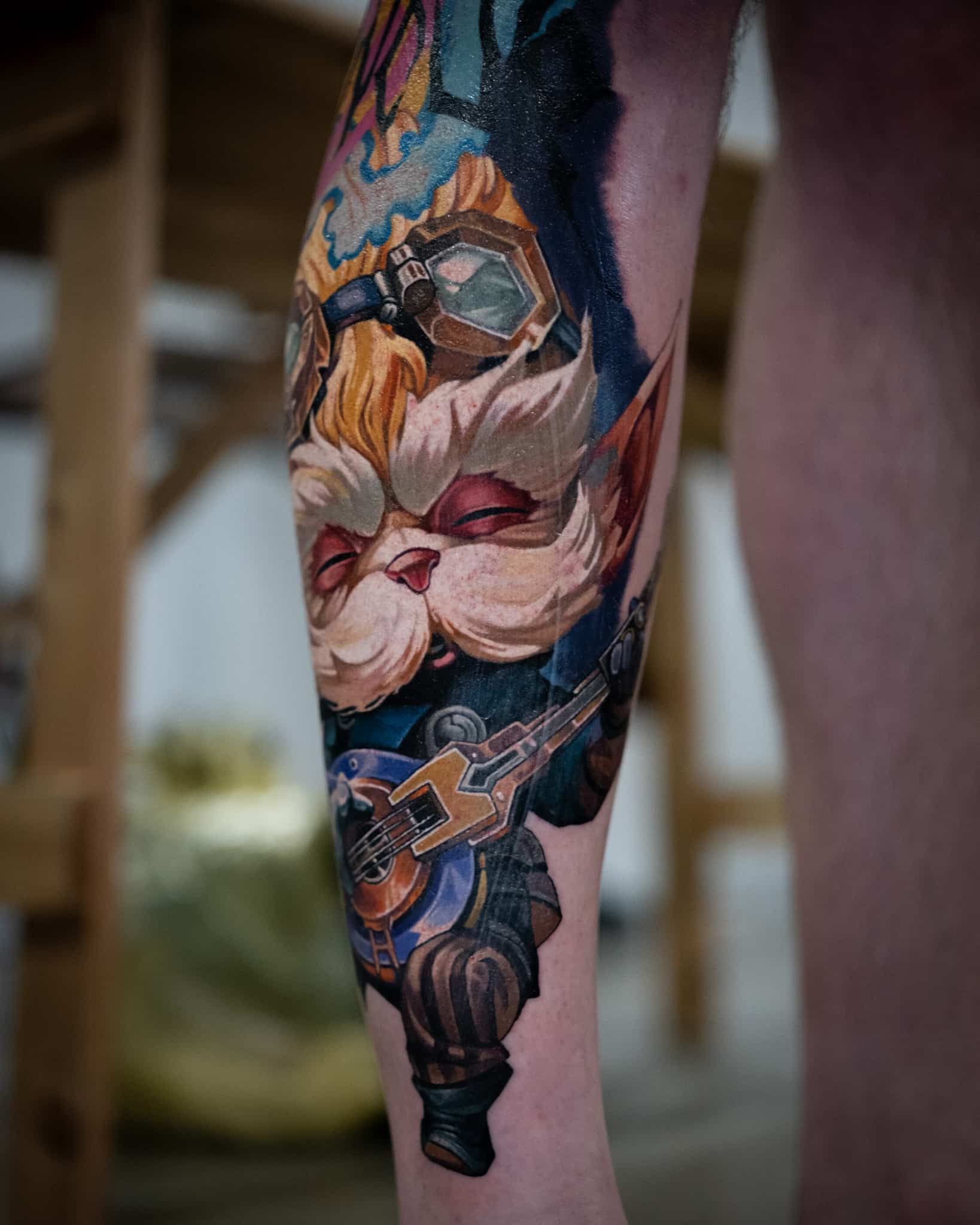 A colorful tattoo on a leg featuring a whimsical, furry creature with goggles playing a small stringed instrument.