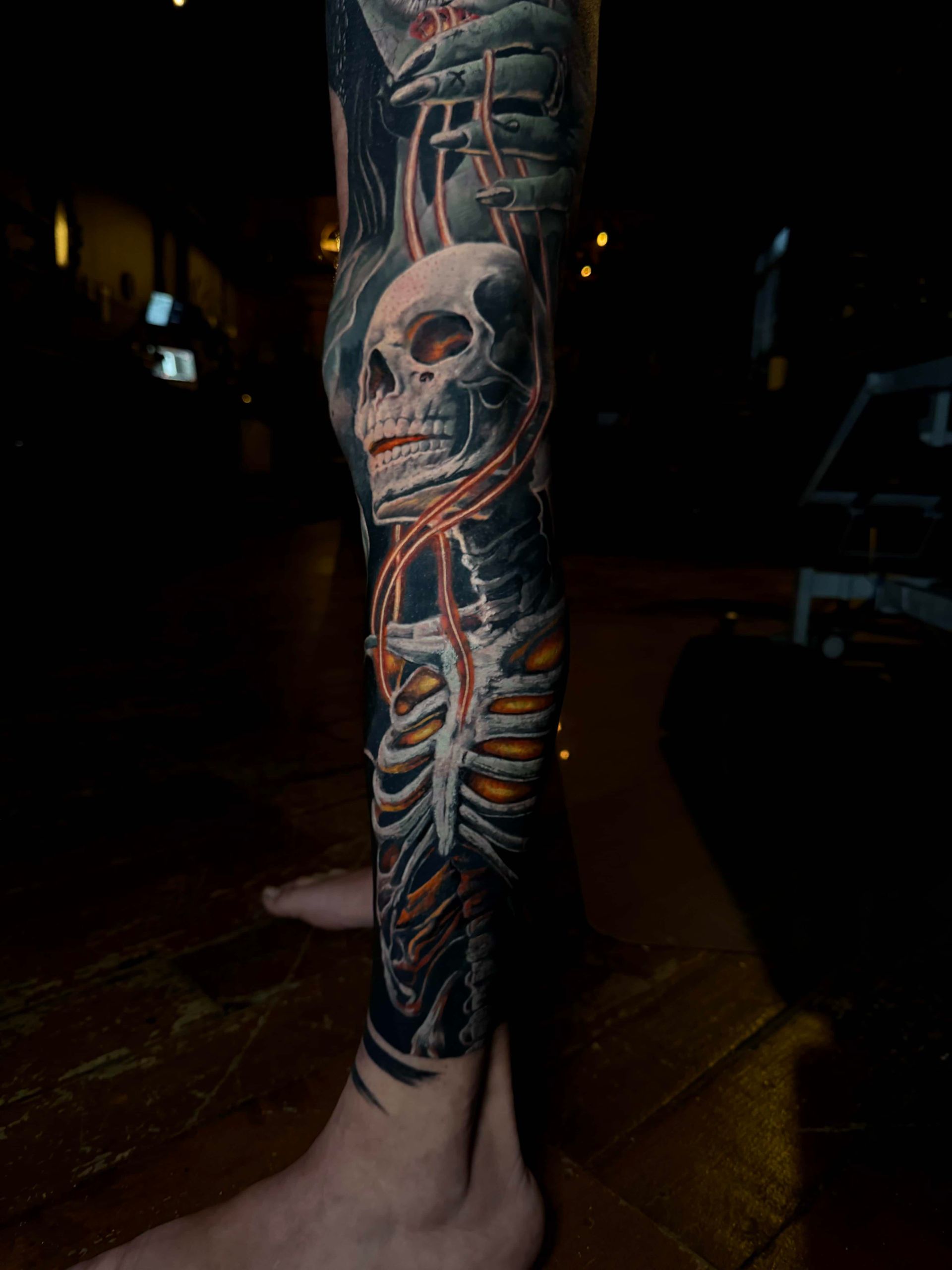 A detailed leg tattoo featuring a skull and ribcage skeleton with glowing orange chain accents on a dark background.