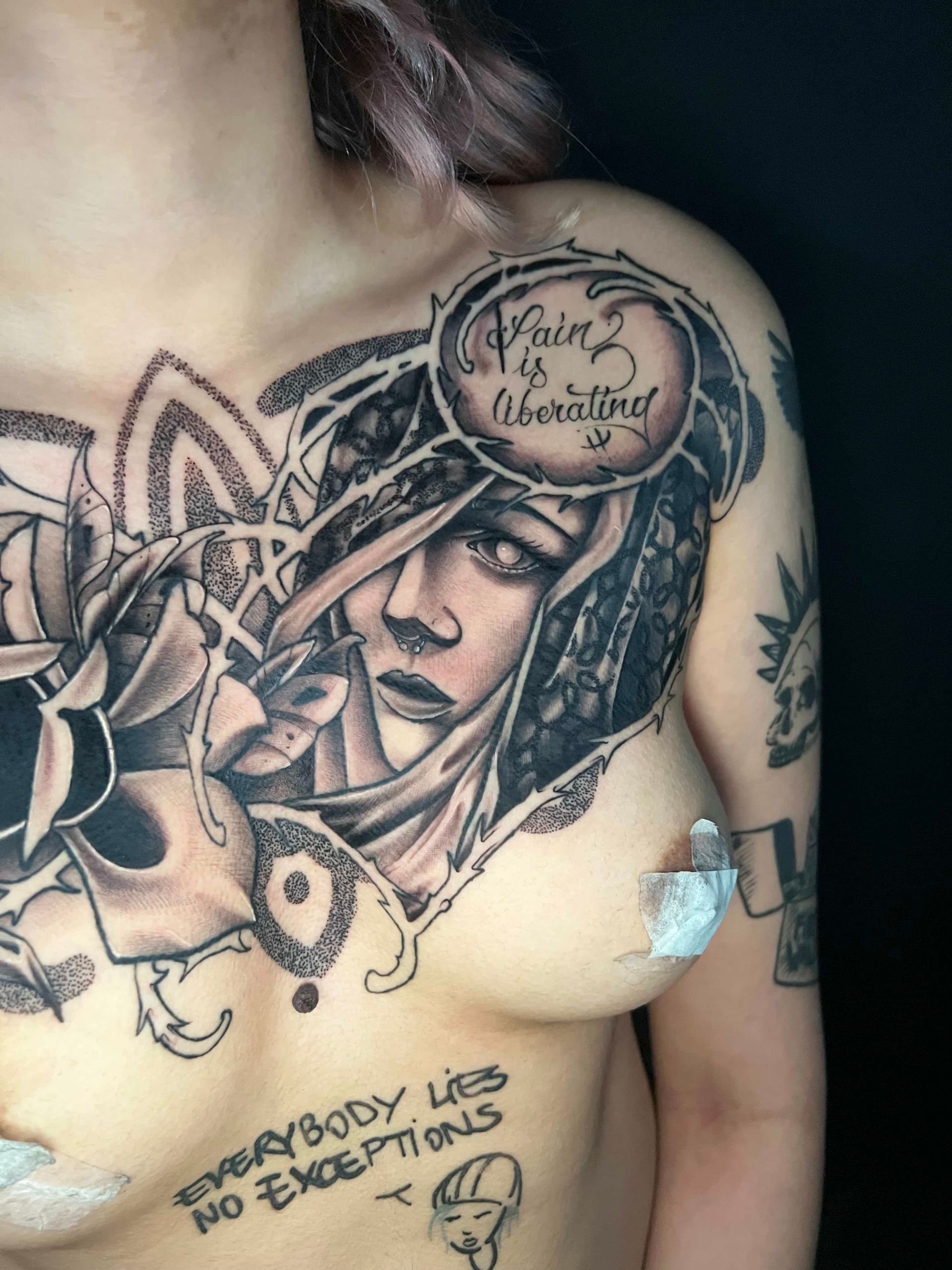 A chest tattoo featuring a portrait surrounded by intricate patterns and text, including 