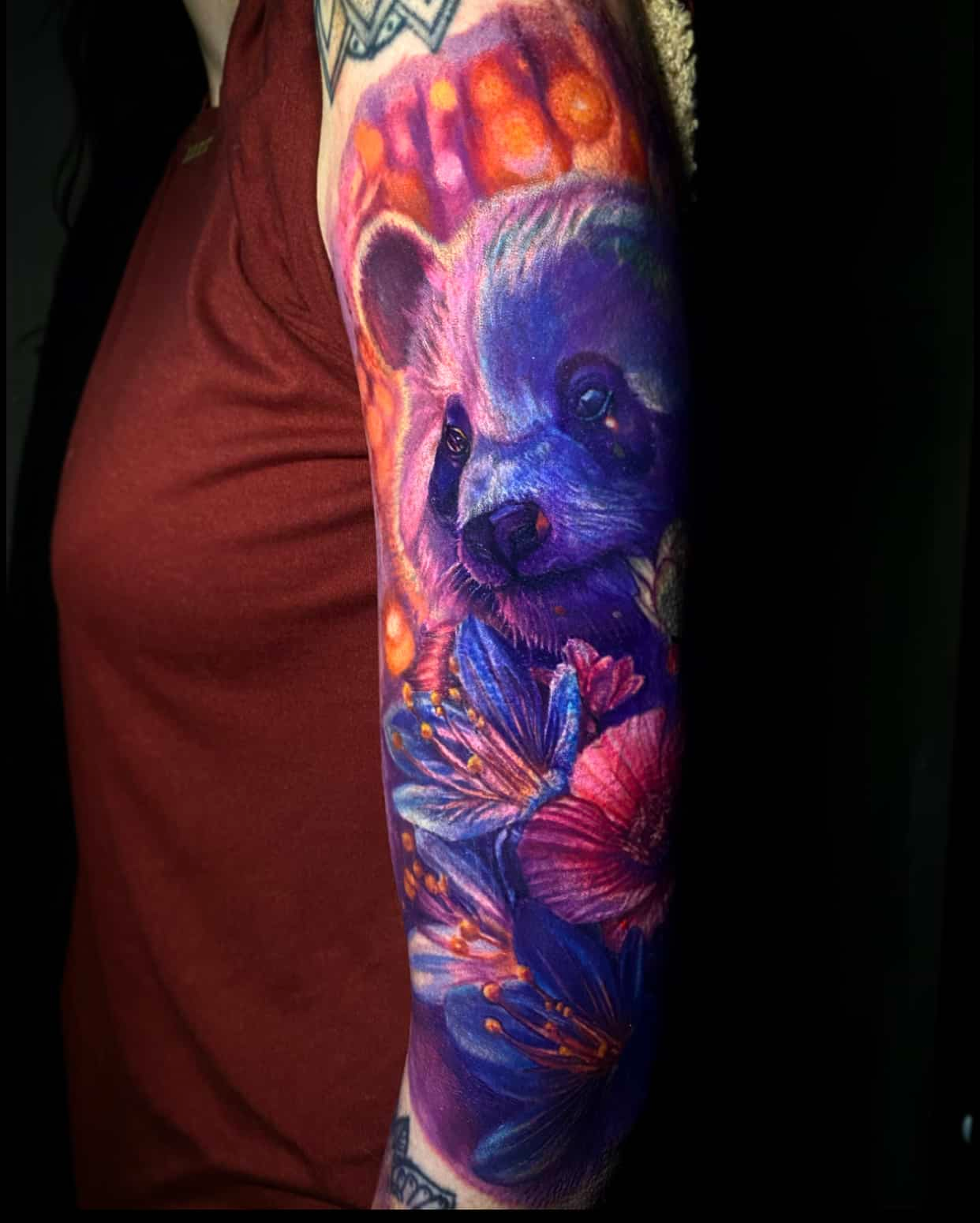A vibrant, colorful tattoo on an arm featuring a panda portrait surrounded by purple and pink flowers.