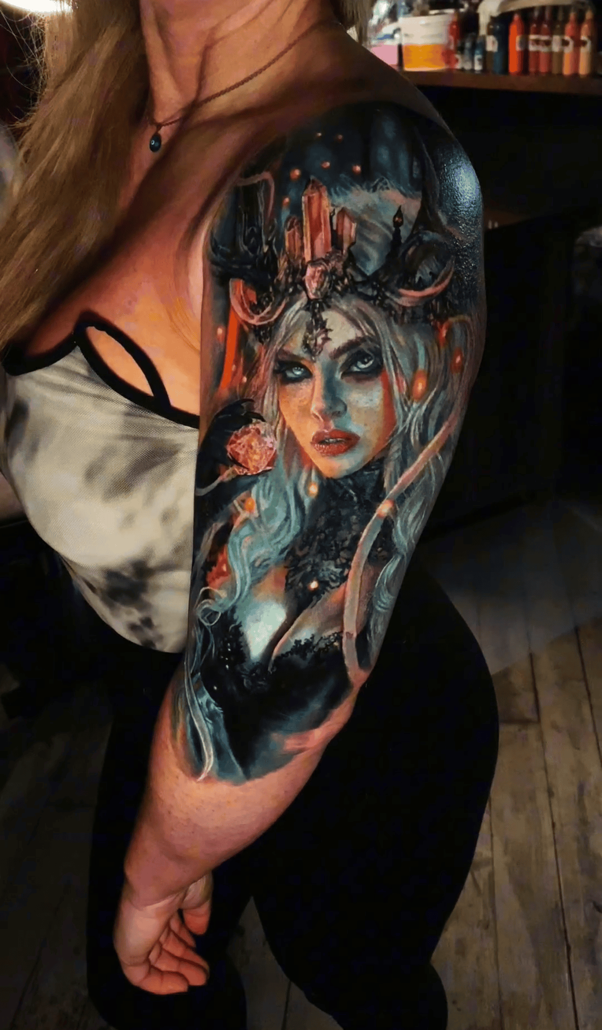 A detailed, colorful upper arm tattoo featuring a woman with light hair, surrounded by dark, atmospheric fantasy elements.