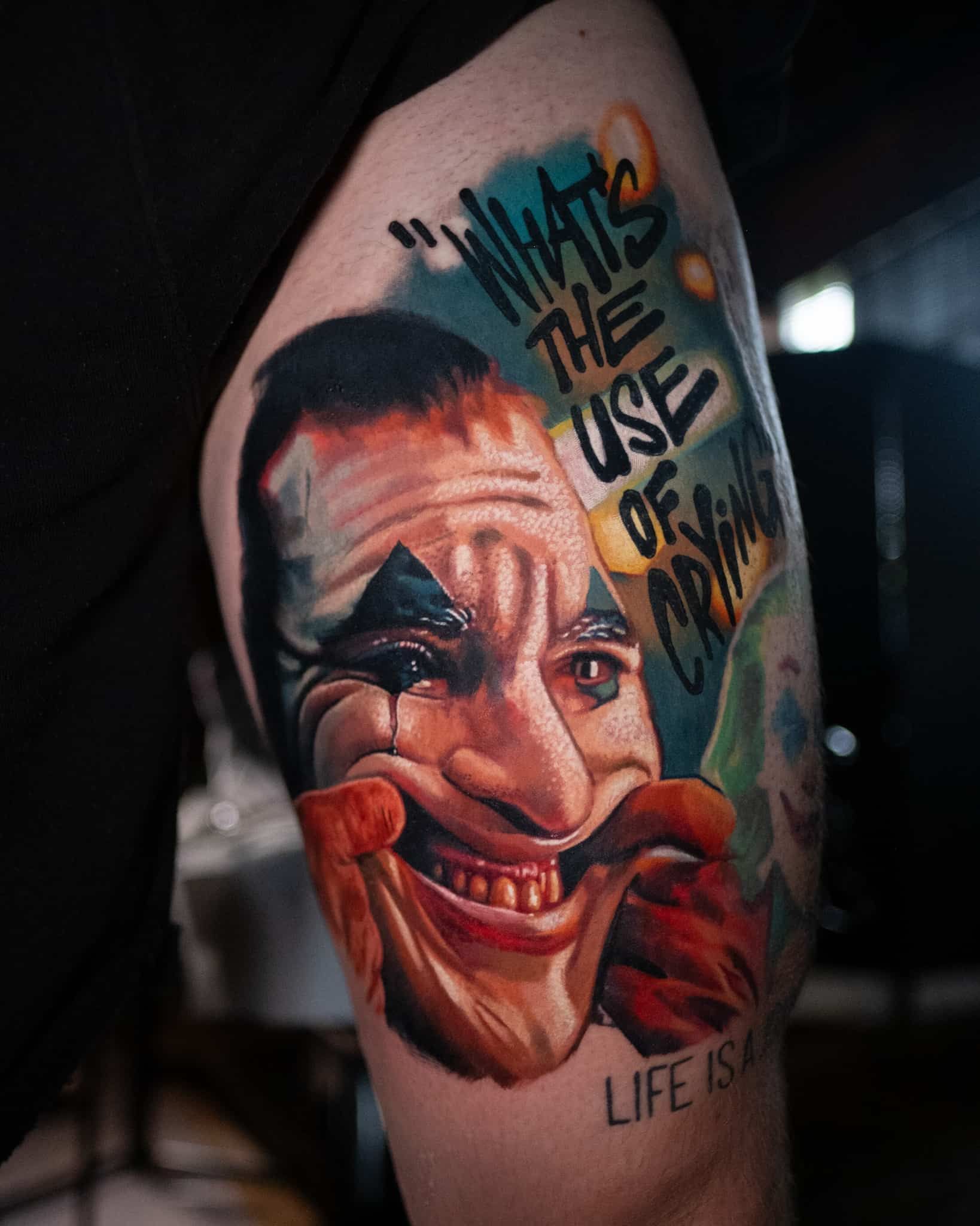Close-up of a color tattoo depicting a clown face with the quote, 