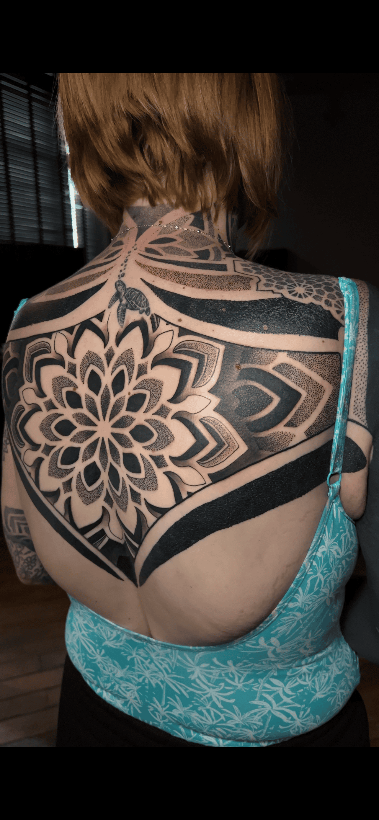 A person viewed from behind featuring an elaborate, symmetrical black-ink mandala tattoo covering their upper back and neck.