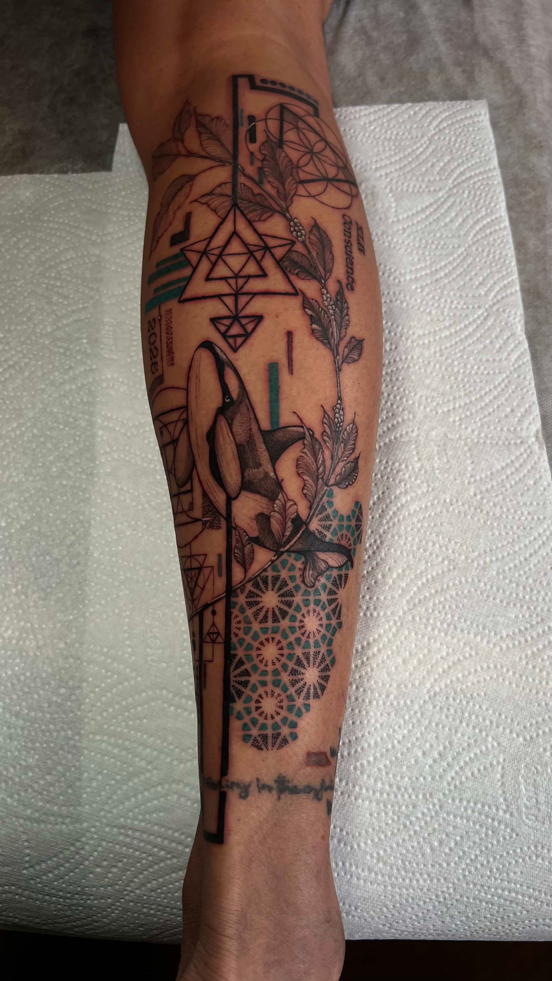 Lower leg tattoo featuring black ink geometric shapes, intricate floral line art, and a repeating mandala pattern.
