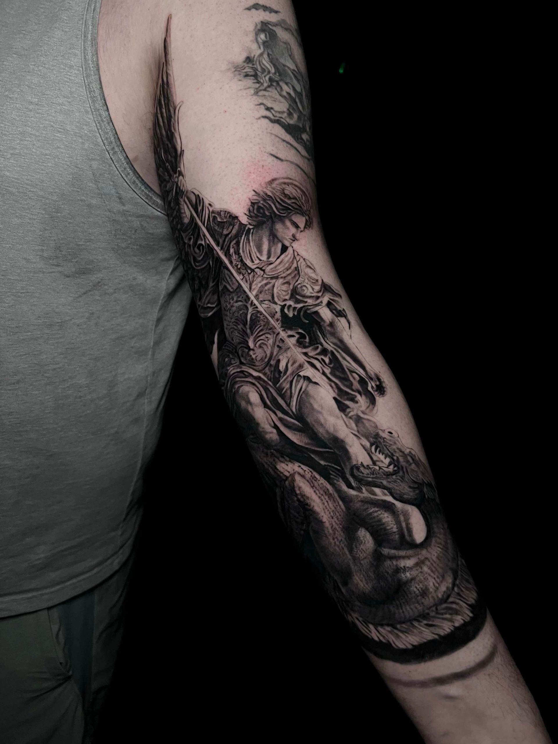 A black and gray tattoo on a person's upper arm featuring detailed, dark, surreal, and flowing artistic imagery.