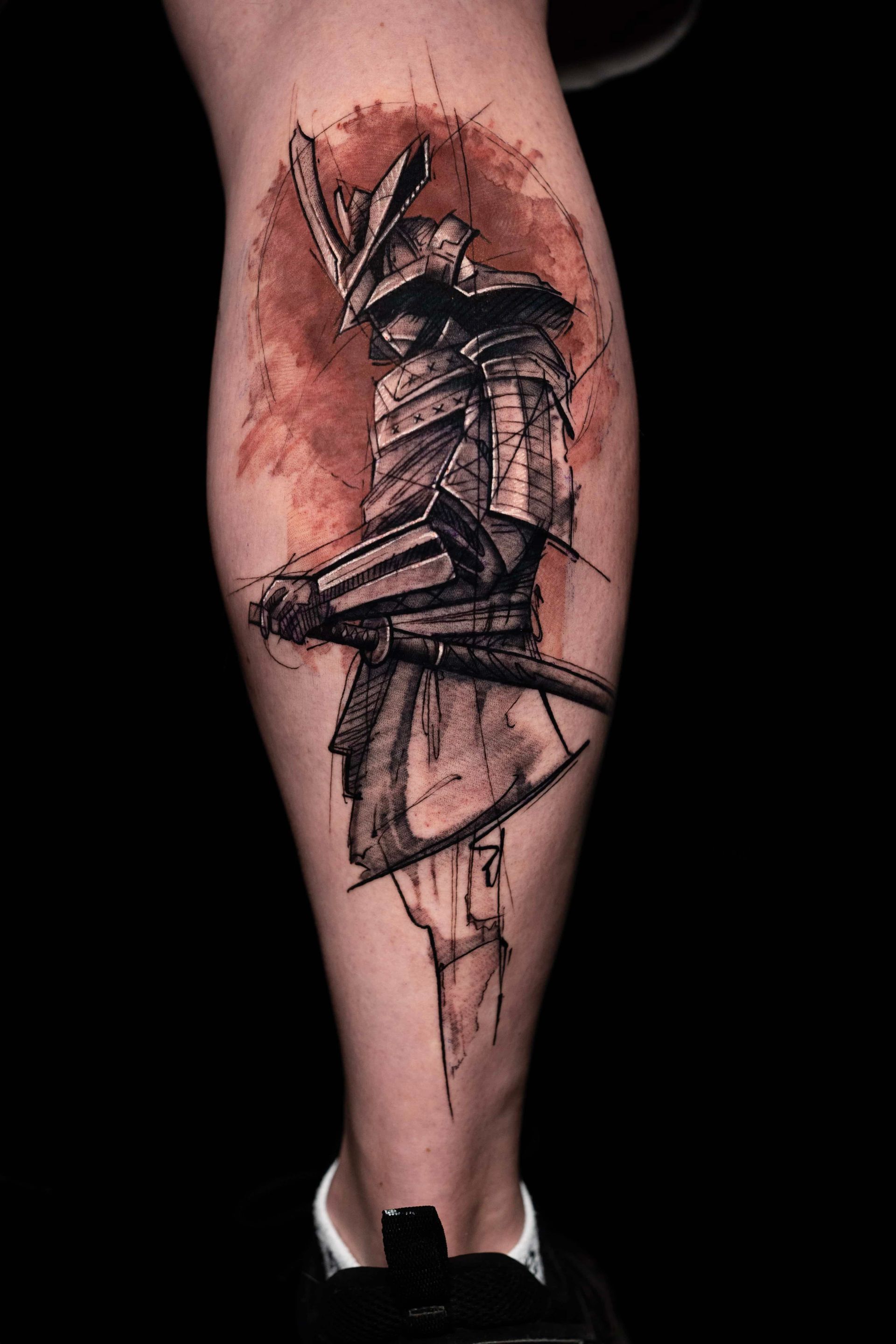 A sketch-style samurai tattoo on a lower leg, featuring dark ink details and a warm, reddish watercolor-style background.