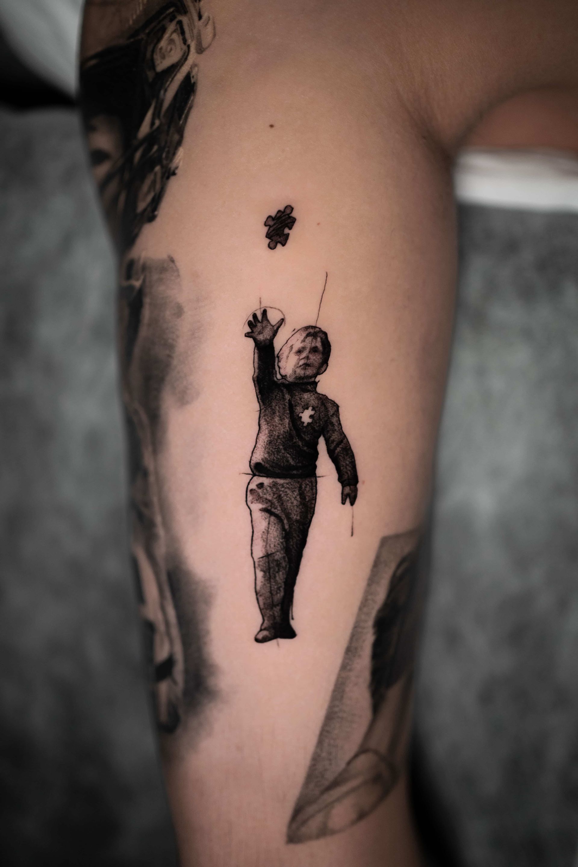 A tattoo on a person's arm showing a figure reaching upward toward a small, dark, cloud-like shape floating above.