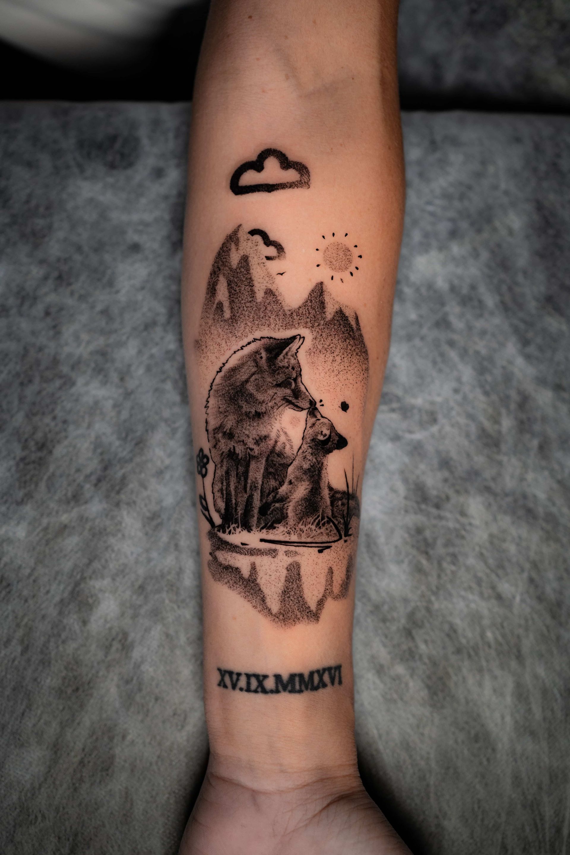 A forearm tattoo featuring a wolf, mountain landscape, sun, and cloud, with the Roman numeral date XV.IX.MMXVI below it.