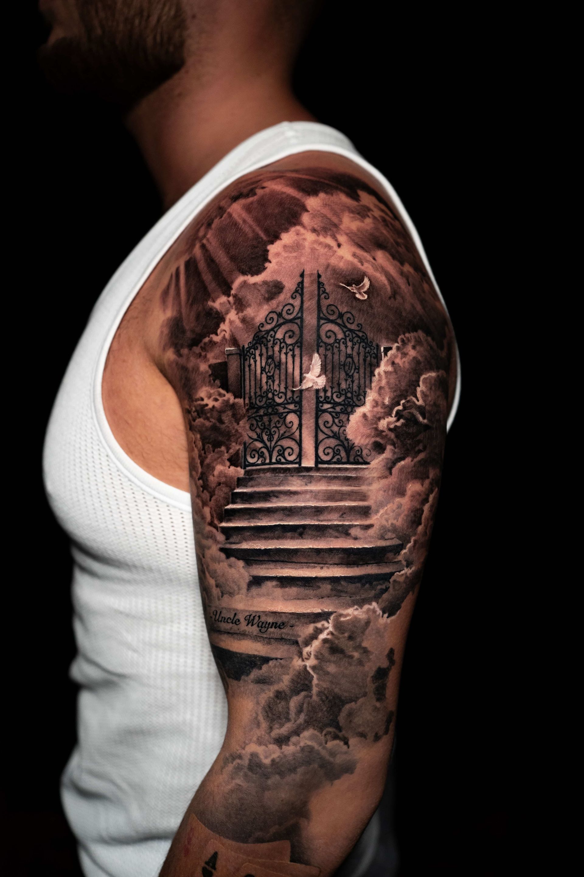 A black-and-grey tattoo on an arm depicting a staircase leading to iron gates surrounded by clouds and doves.