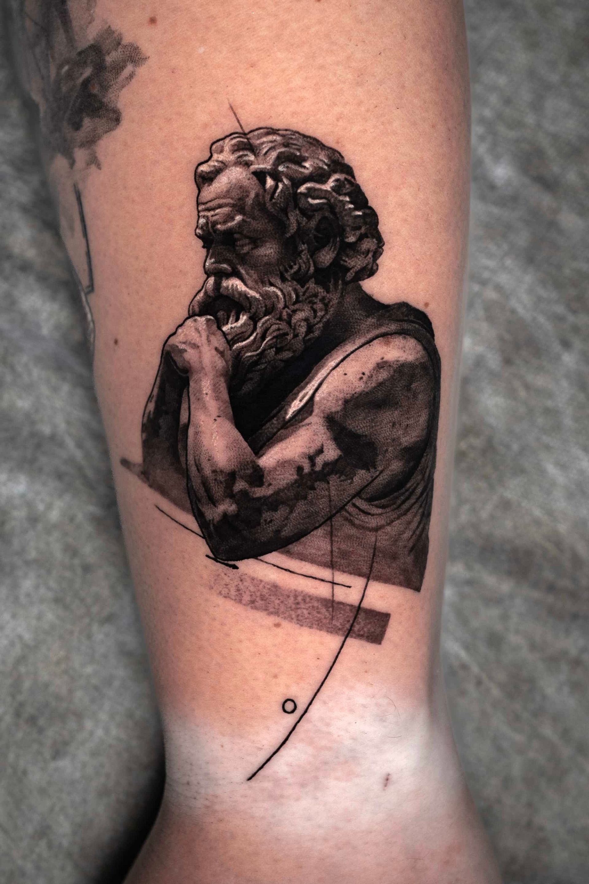 A realistic tattoo on an arm depicting the bust of a bearded, pensive man, accented by abstract geometric lines.