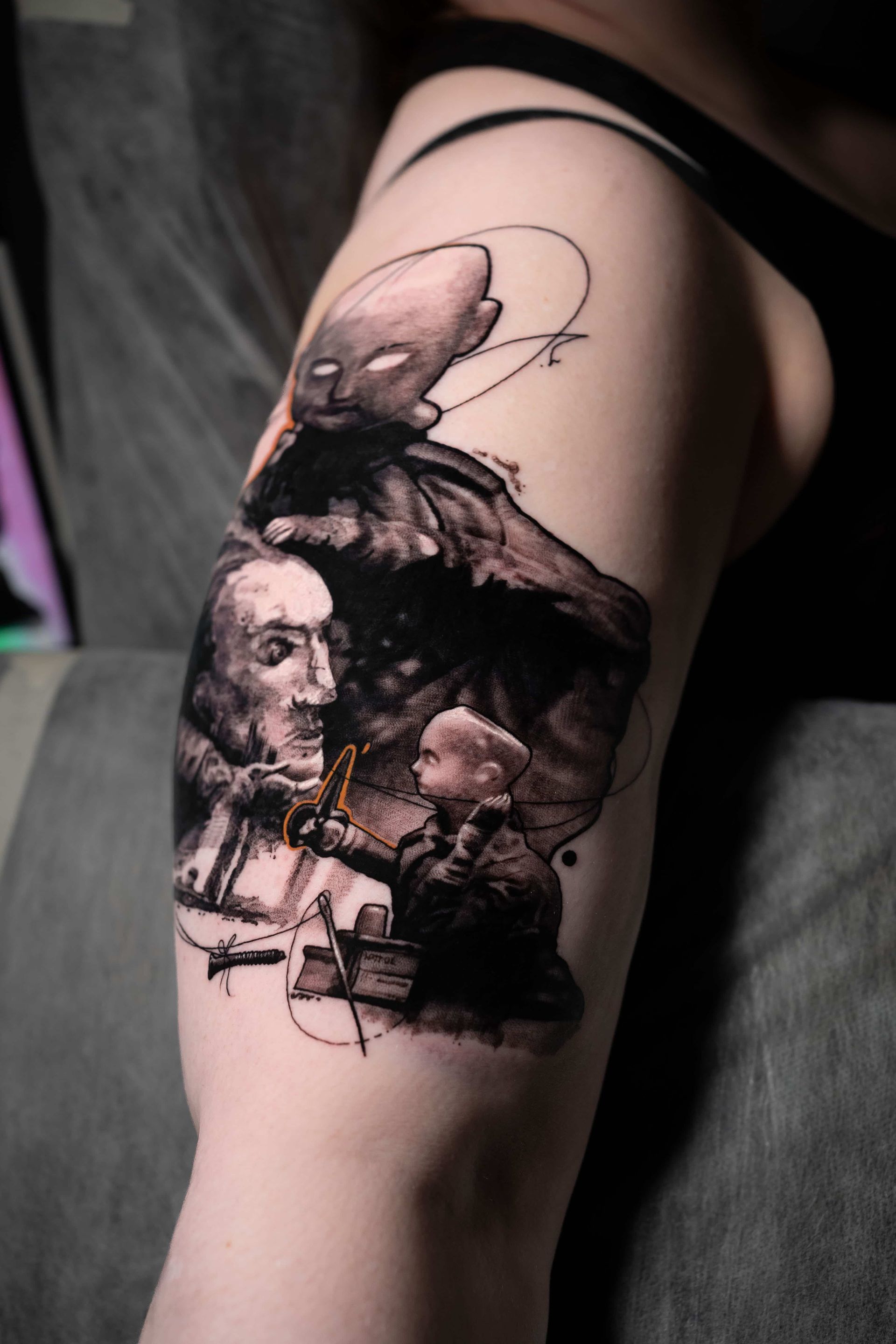 A black-and-grey tattoo on an upper arm featuring an etched-style depiction of faces and hands with abstract linework.