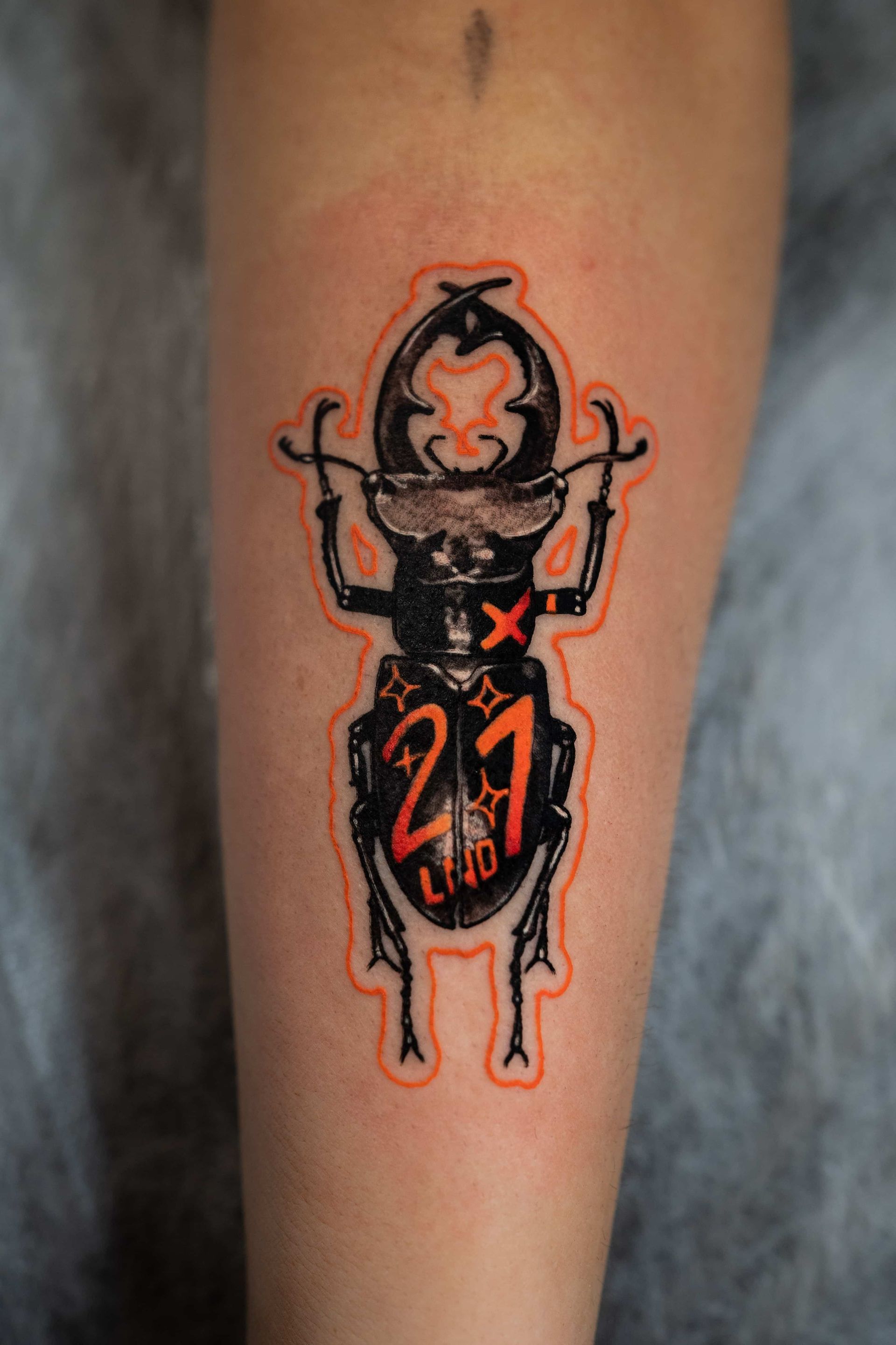 A tattoo on a forearm of a black stag beetle with orange accents, the number 
