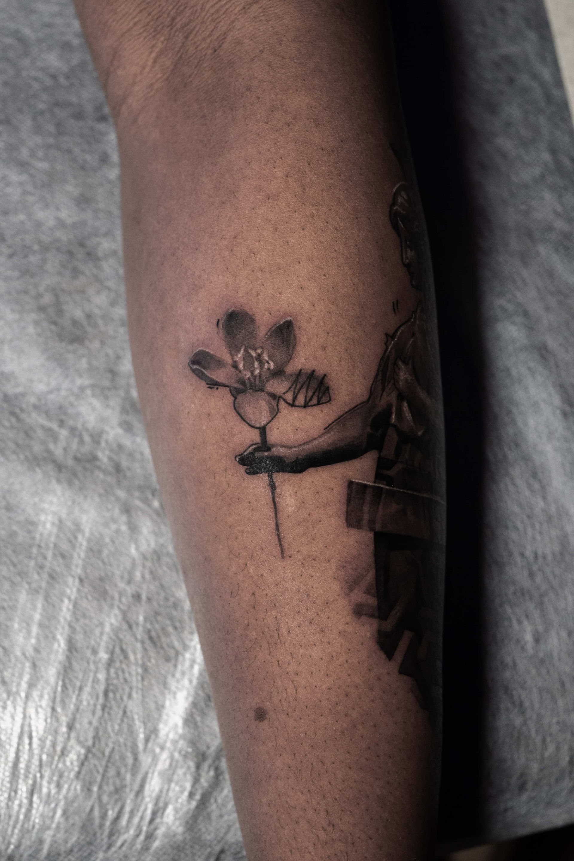 A black-and-grey tattoo on skin depicting a figure holding a flower.