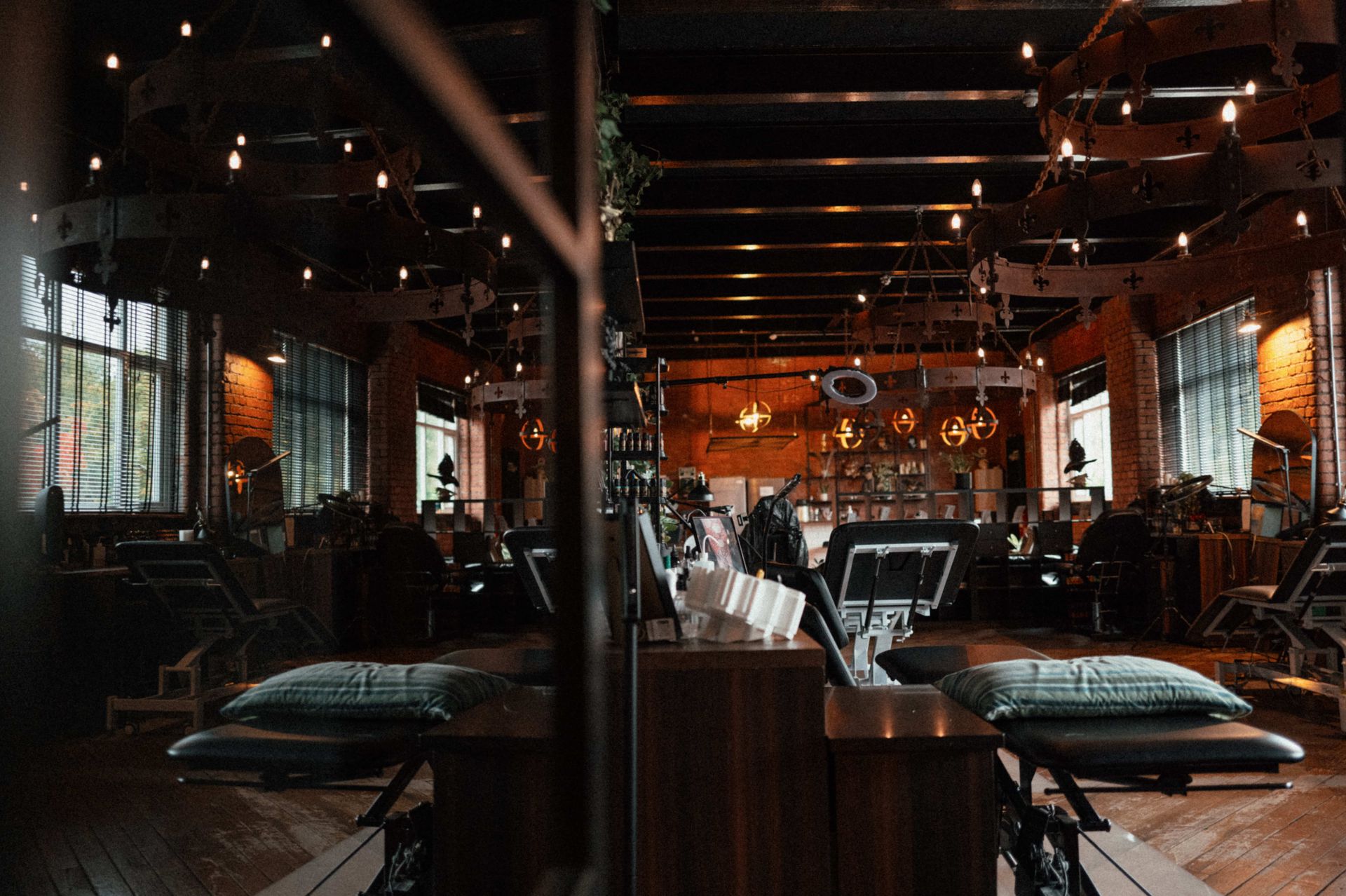 A professional tattoo studio with dark wood floors, dim lighting, and several treatment chairs arranged in rows.