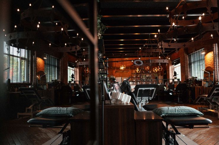 A professional tattoo studio with dark wood floors, dim lighting, and several treatment chairs arranged in rows.