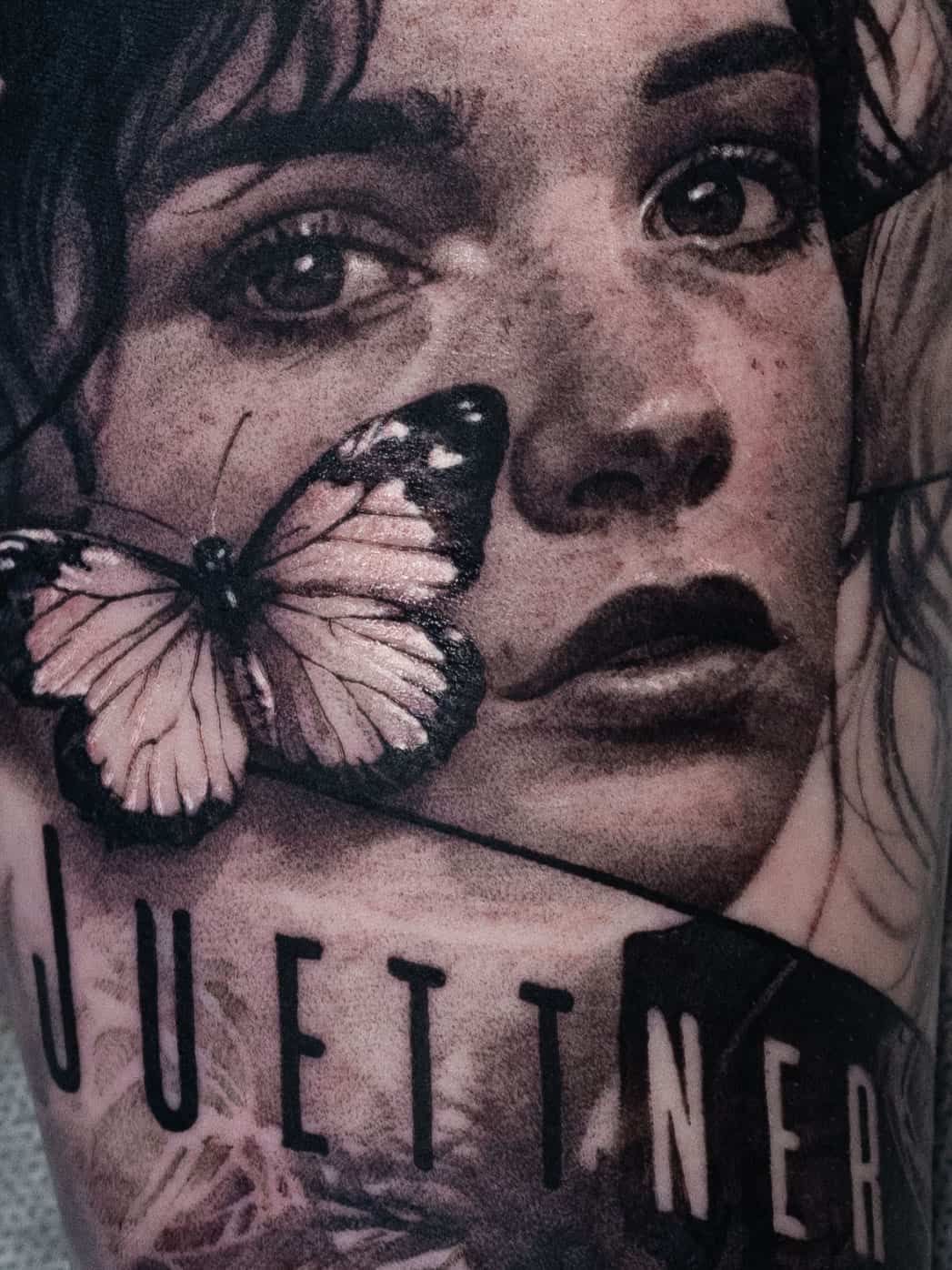 A detailed, black-and-grey tattoo of a person’s face with a butterfly over one eye and the word 