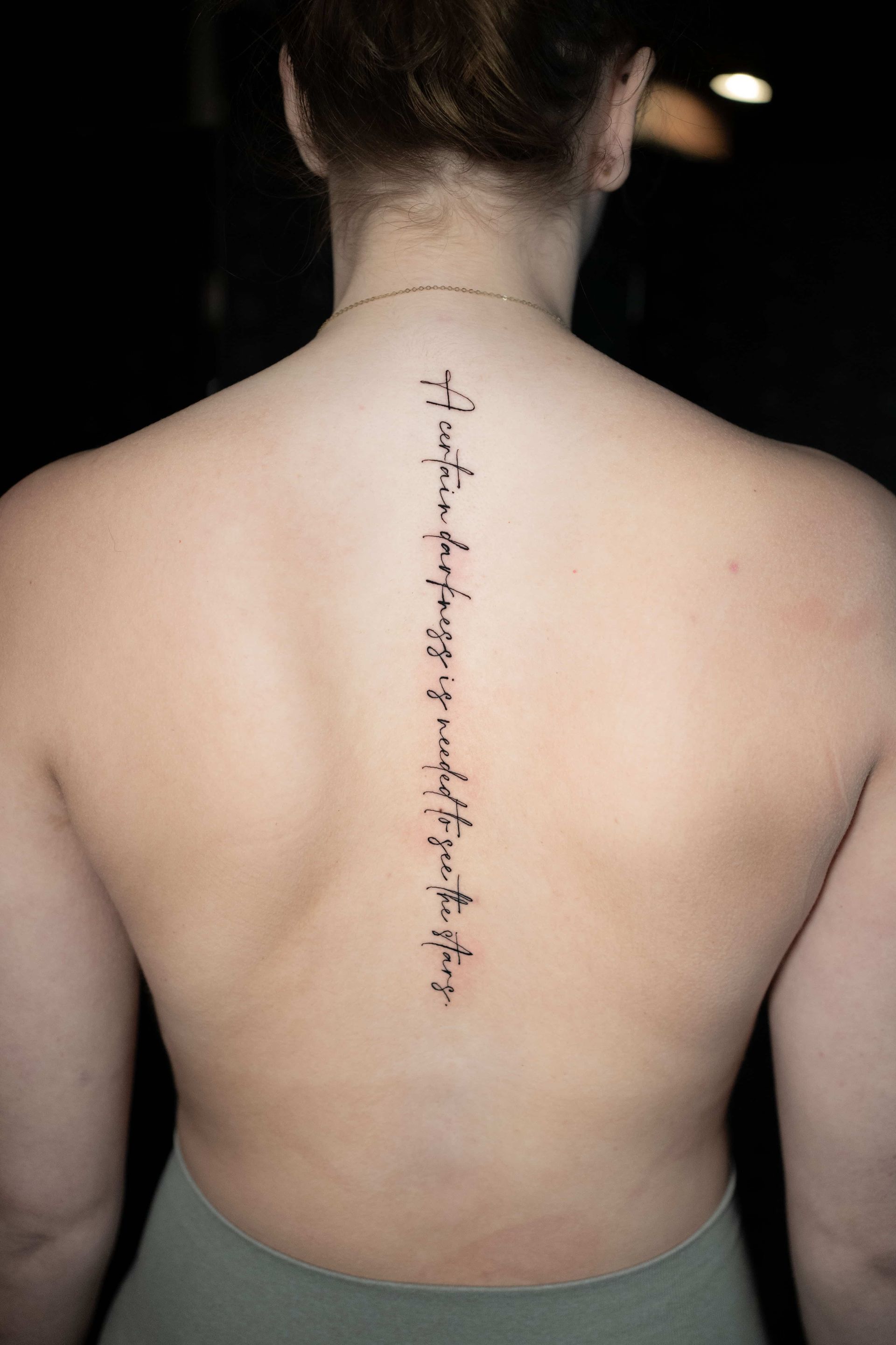A back view of a person with a long, thin, vertical script tattoo running down the center of their spine.