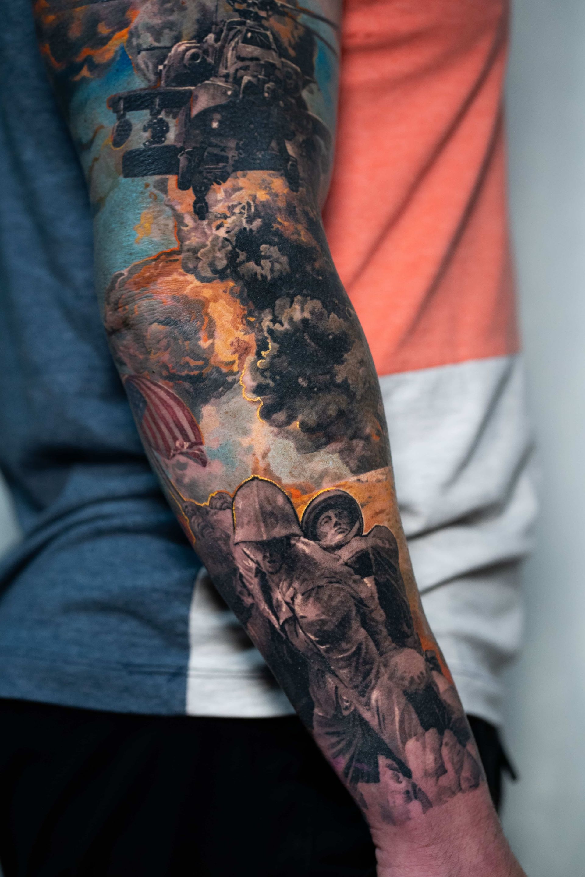 A detailed tattoo on a person's forearm featuring a military helicopter, dark clouds, and soldiers in combat gear.