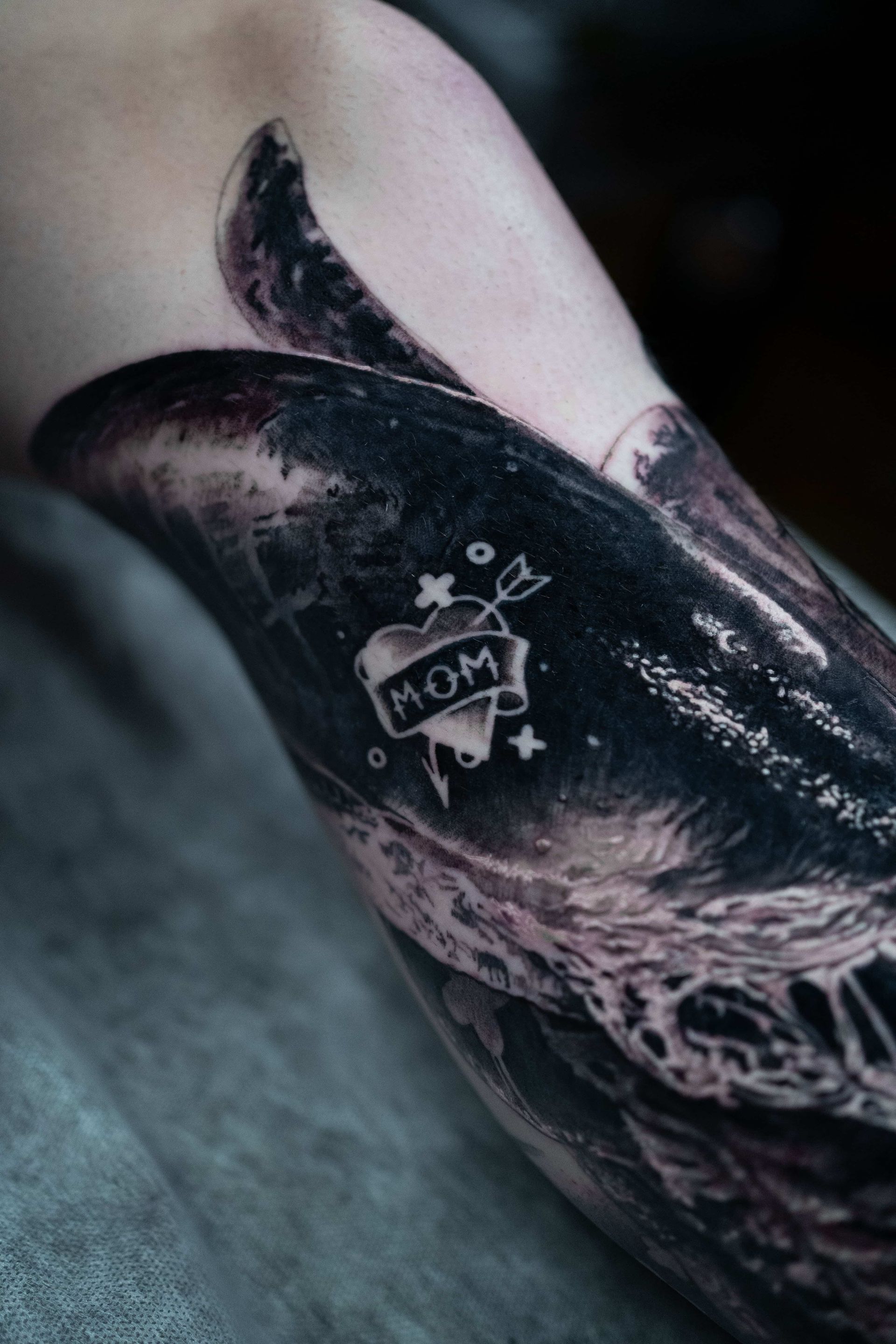 A close-up of a person's arm showing a small, white-ink heart tattoo with the word 