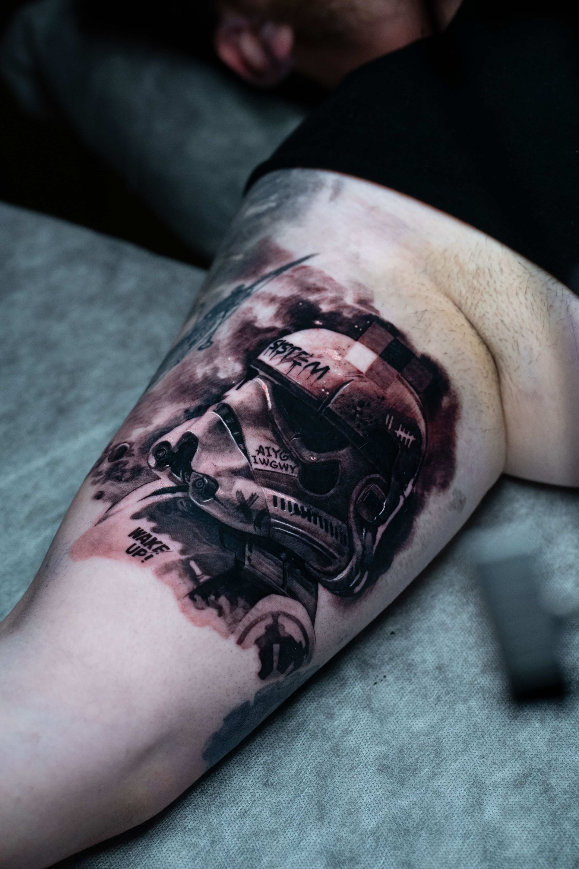 Detailed tattoo of a weathered Star Wars Stormtrooper helmet on an upper arm, featuring dark, smoky, abstract shading.