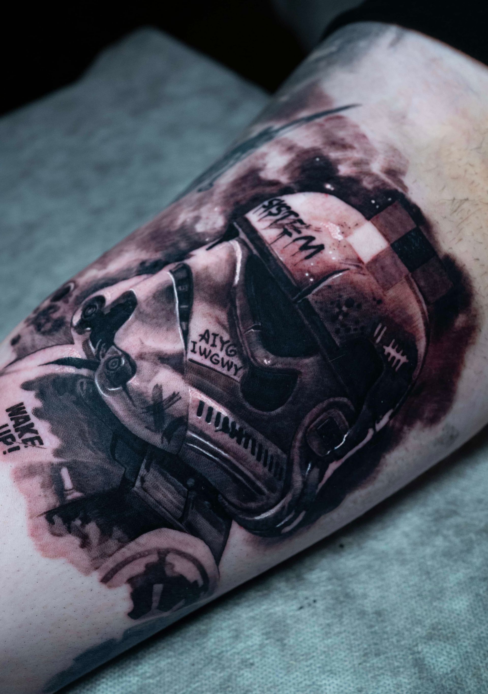 A black-and-grey tattoo on skin showing a weathered, battle-worn Star Wars stormtrooper helmet with text.